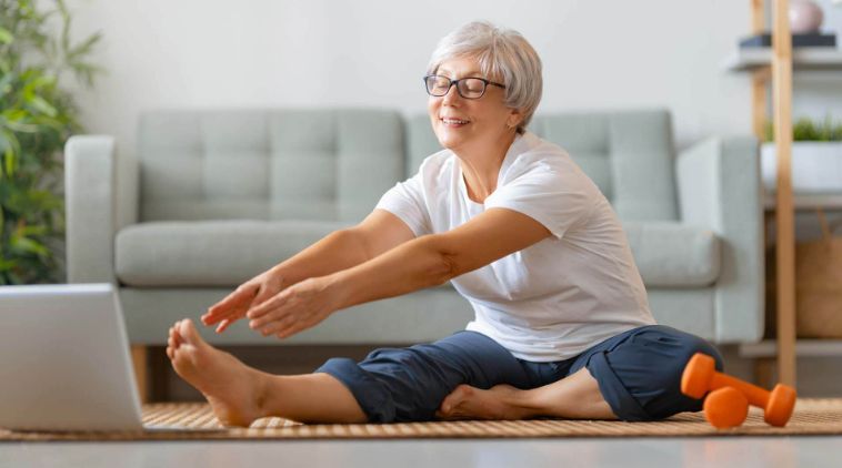 An older woman stretching on an exercise mat at home